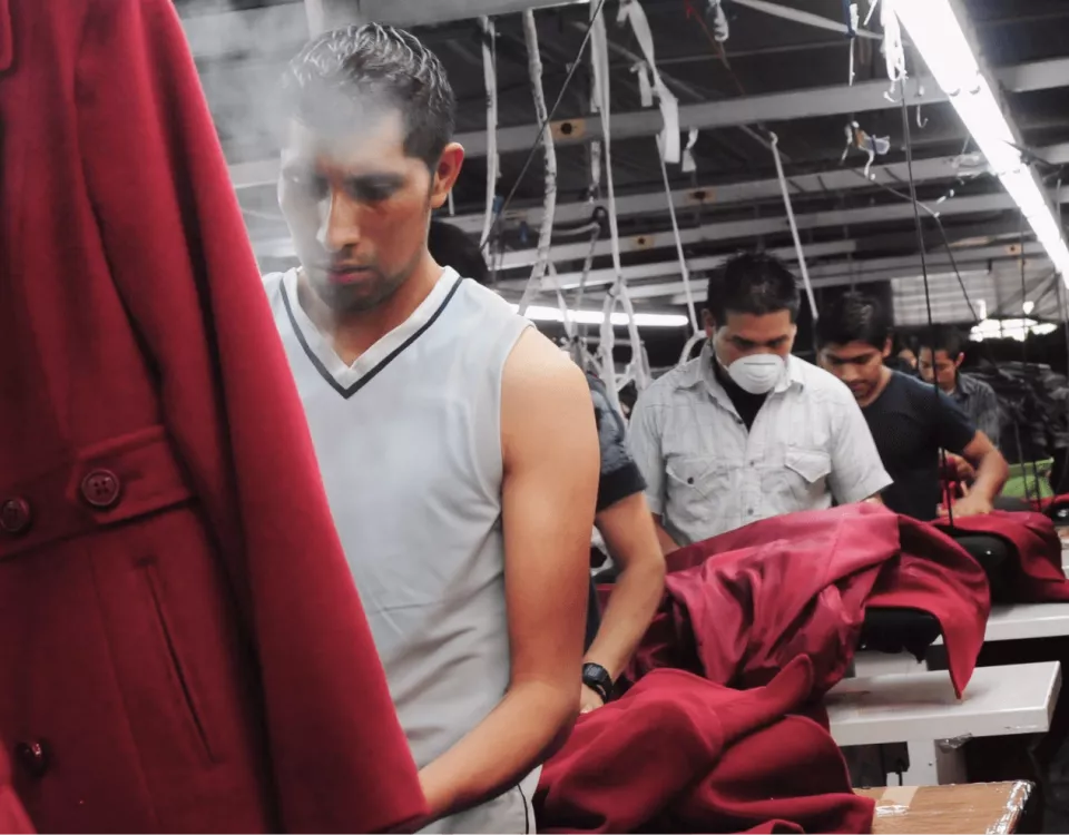 The image shows a man in a factory steaming a red coat