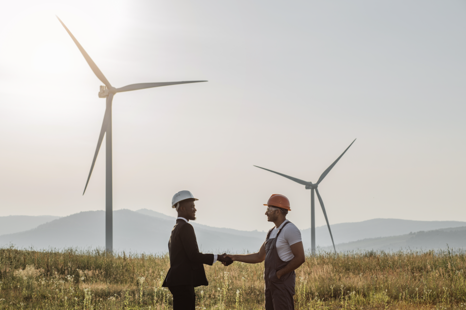Two men shaking hands with two windmills in the background