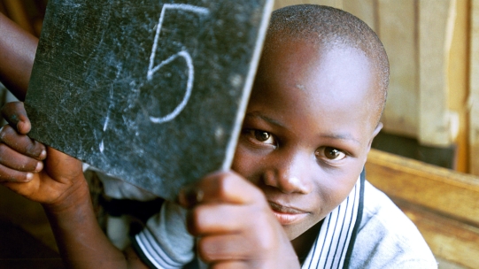 Child holding up number 5 on a chalkboard